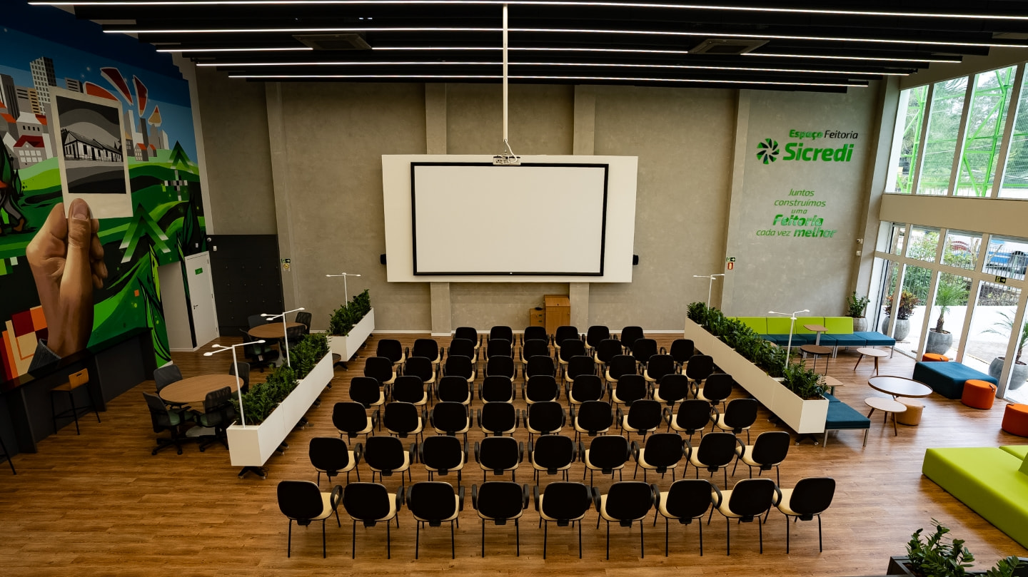 Auditório com capacidade para até 106 pessoas sentadas, com cadeiras e arquibancadas, equipado com tela para projeção de 200 polegadas