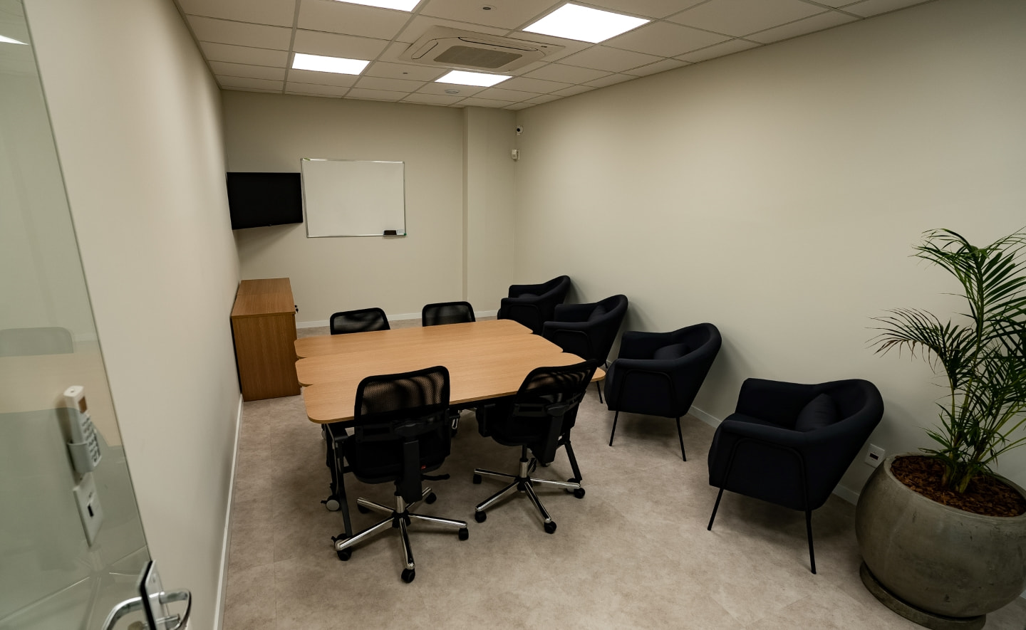 Sala de Reuniões equipada com mesa, cadeiras, televisão, quadro branco e poltronas